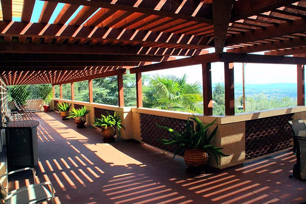 Covered veranda with wooden pergola, comfortable seating, potted plants, and panoramic views overlooking the San Gabriel Valley at Mater Dolorosa Passionist Retreat Center.